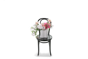 Wide image of white wave ceramic vase design. White vase ceramic vase, displaying mixed pink flowers and seasonal foliage. Vase design is sitting on a black bentwood chair with white background.