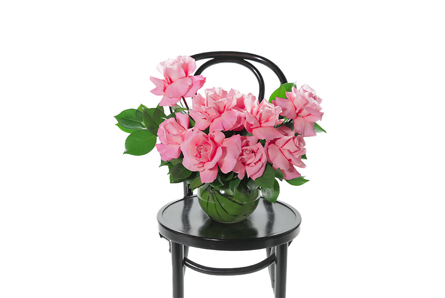 HATTIE vase design is timeless vase design that displays Reflexed pink Roses and a hint of green seasonal foliage, designed into a premium leaf lined ball vase. HATTIE vase design is sitting on a black bentwood chair. Packed full of beautiful roses and includes the vase. Vase design is presented into a Kate Hill flower bag and detailed with ribbon for gifting.