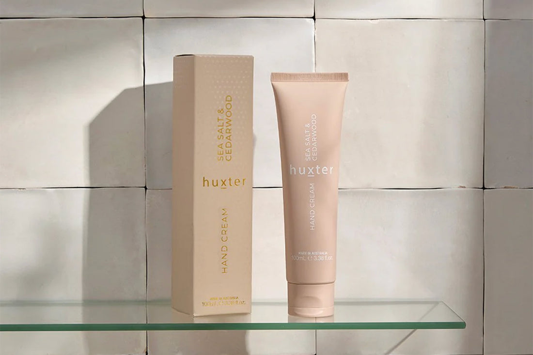 Huxster hand cream and box on a glass shelf with a tiled wall background.