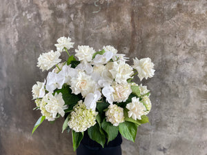 Wide image of Large white and green casket tribute design, being held by a florist wearing black and standing in front of a concrete wall.