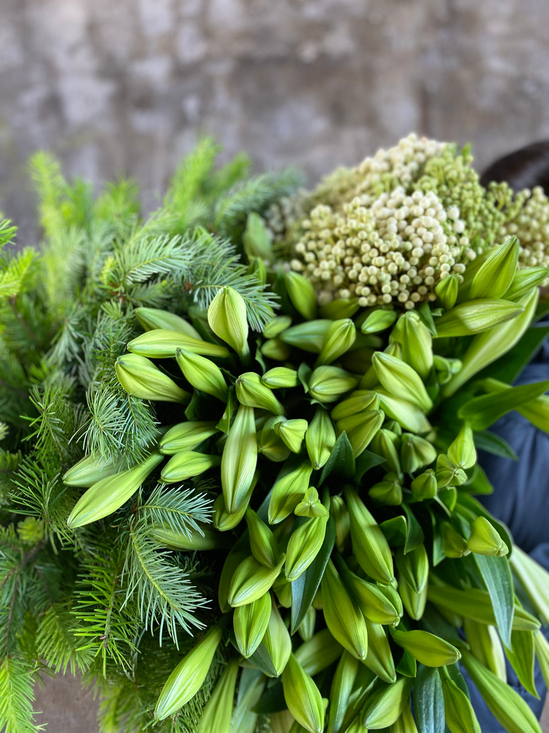 A large bundle of Christmas flowers and foliage being held by a florist, against a concrete wall.