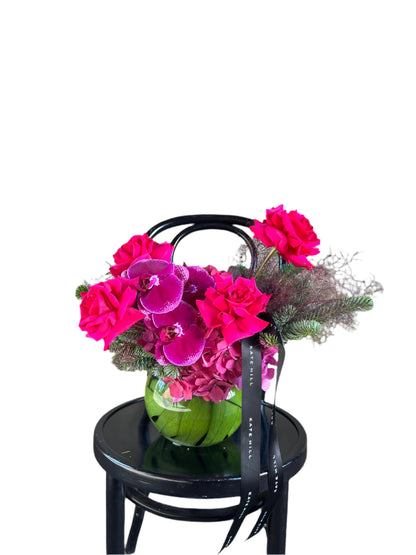 A jewel toned ball vase design sitting on a black bentwood chair with a white wall background.