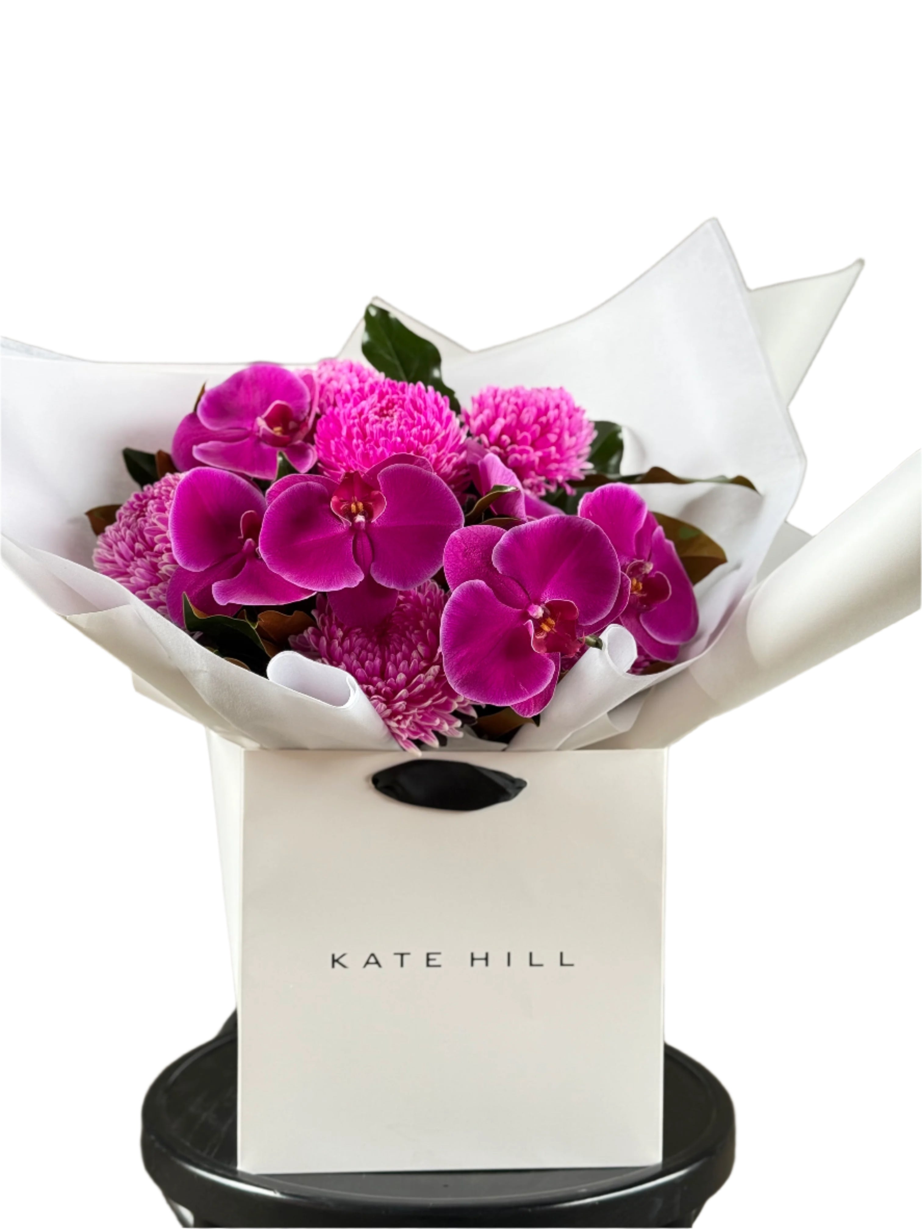 Close up image of a vibrant hot pink and magenta flower bouquet, presented in our signature white wrapping and flower bag. Bouquet bag is sitting on a black bentwood chair with a white background.