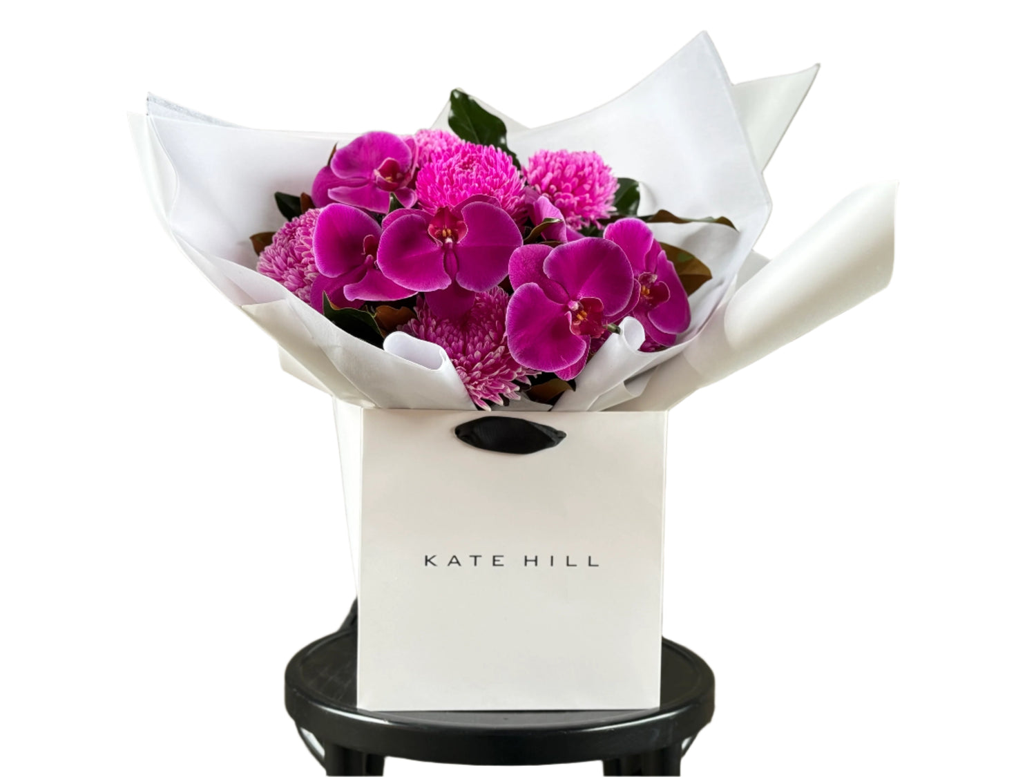 Close up mage of our May Birthday Bouquet. A vibrant hot pink and magenta flower bouquet, presented in our signature white wrapping and flower bag. Bouquet bag is sitting on a black bentwood chair with a white background.