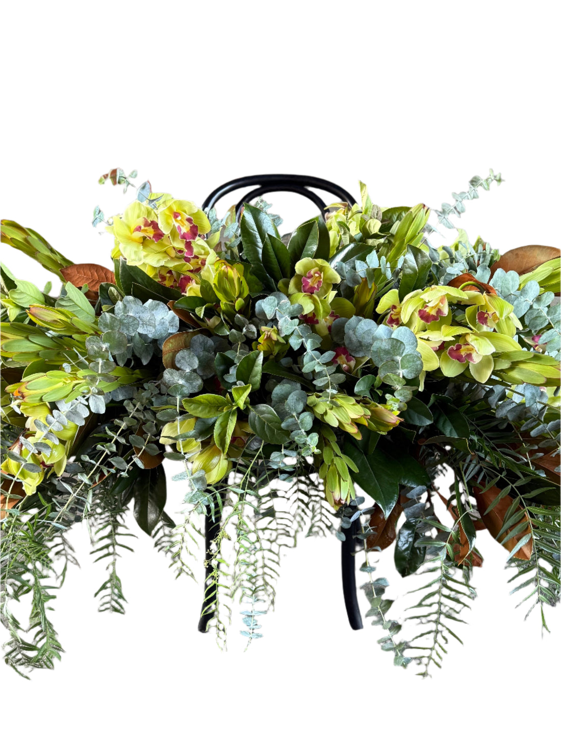 A close up of a green and native funeral casket spray displayed on a black bentwood chair white background.