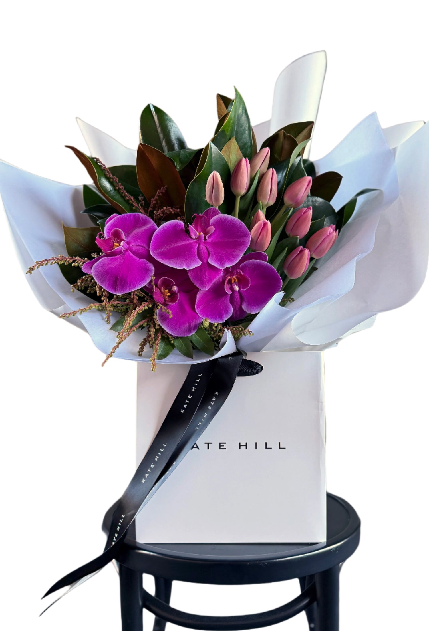 Bouquet of bright pink flowers on a black bentwood chair against a white wall.