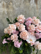 Close up image of Pastel pink, white and green casket design, held by a florist wearing back, up against a concrete wall.