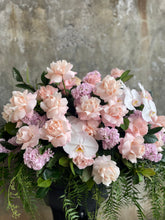 Close Pastel pink, white and green casket design, held by a florist wearing back, up against a concrete wall.