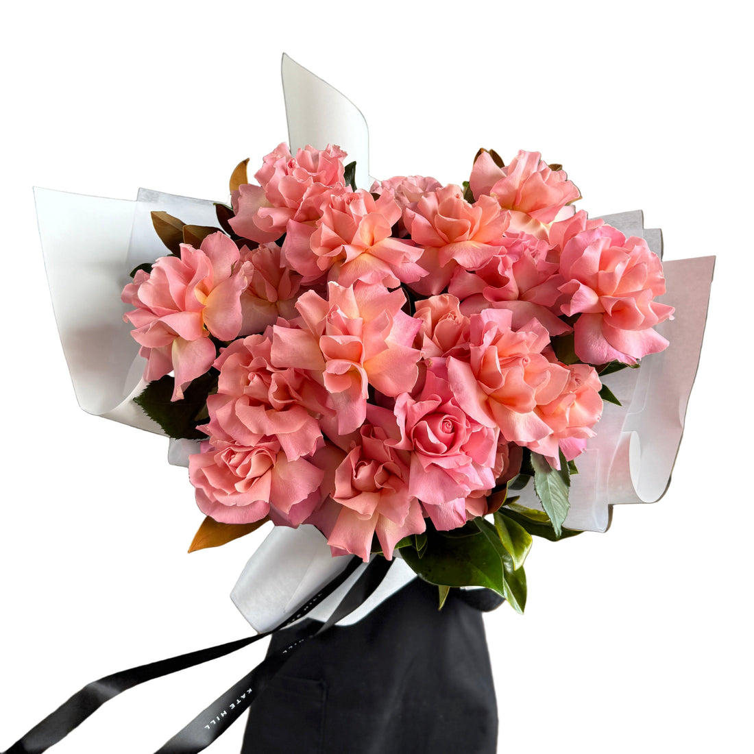 Florist holding a bouquet of watermelon pink rose flowers wrapped in white paper against a white wall background. 