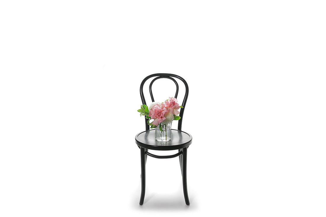 Wide image of a mixed white, pink and green petite vase design sitting on a black bentwood chair with a white wall background.