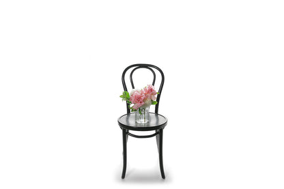 Wide image of a mixed white, pink and green petite vase design sitting on a black bentwood chair with a white wall background.