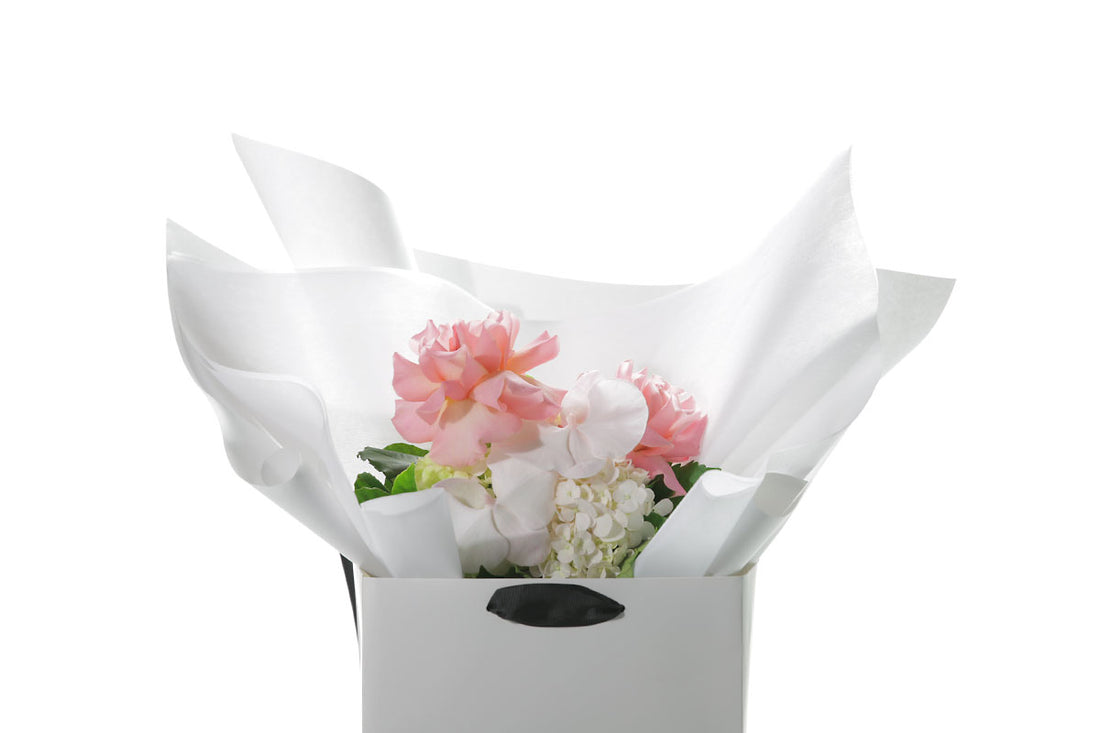 Close up image of a mixed pastel flower bouquet beautifully wrapped in Kate Hill Flowers signature wrapping in our flower bag and sitting on a black bentwood chair with white wall background.