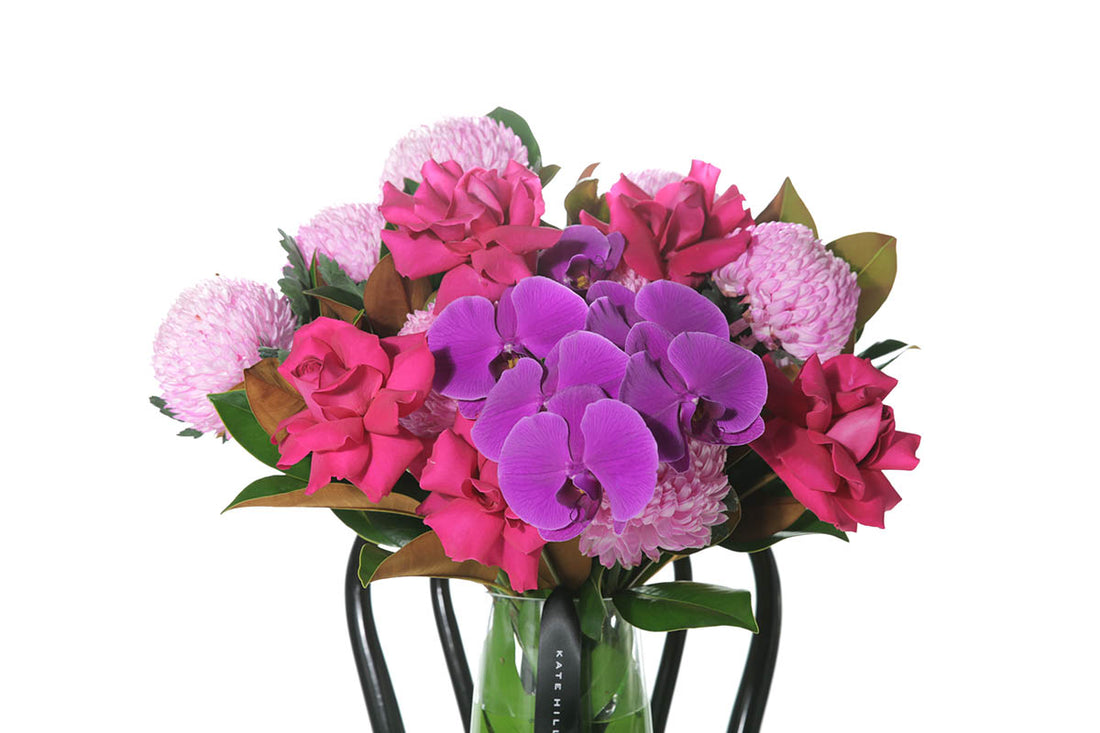 Kate Hill Flowers – large bright-pink and magenta birthday vase with roses, chrysanthemums and orchids in a monstera-lined glass.