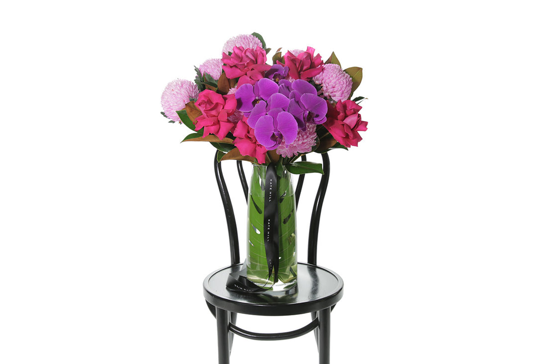 Kate Hill Flowers – large bright-pink and magenta birthday vase with roses, chrysanthemums and orchids in a monstera-lined glass.