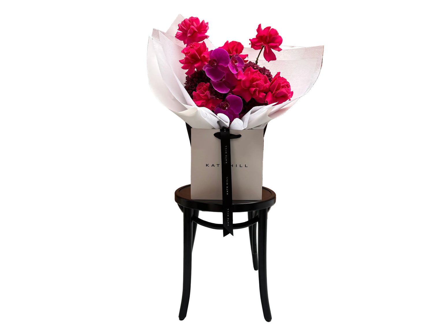 June signature flower bouquet featuring bright pink tones on black chair.