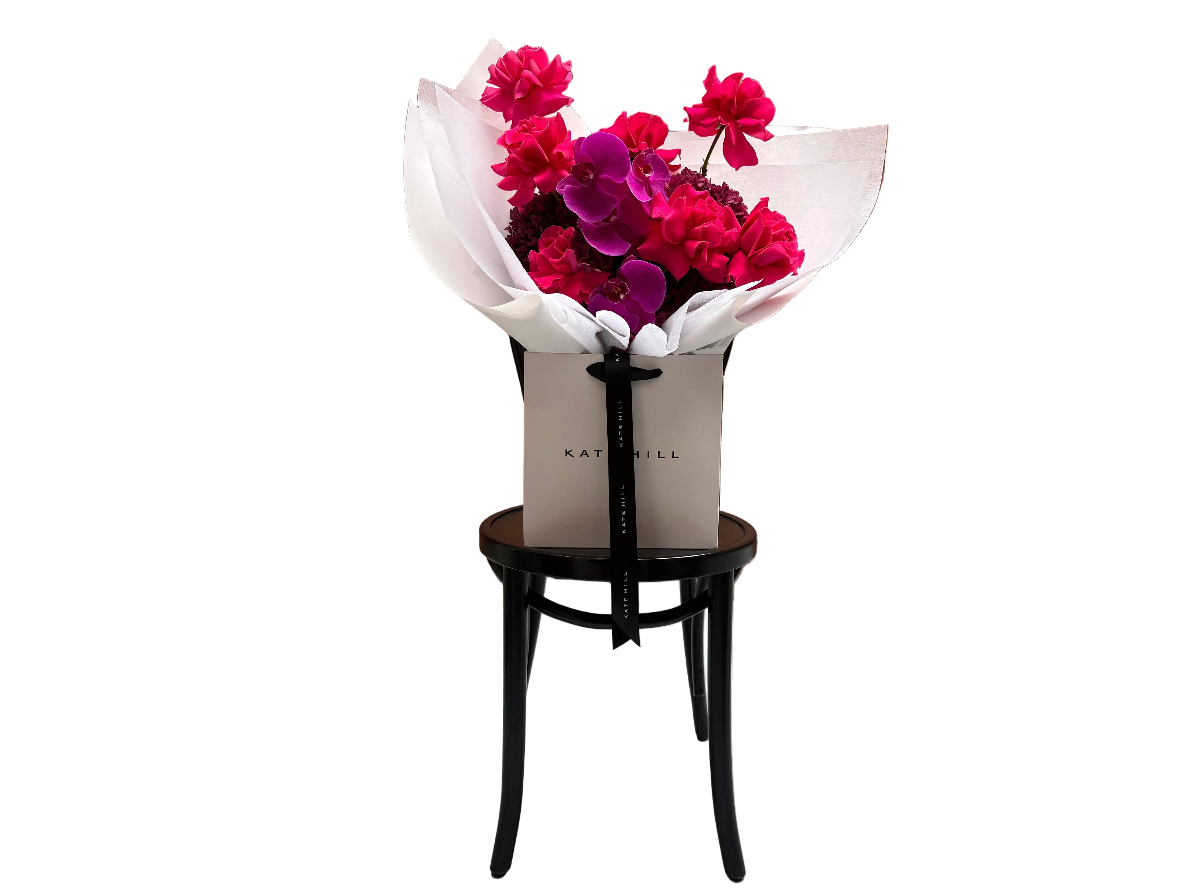 June signature flower bouquet featuring bright pink tones on black chair.