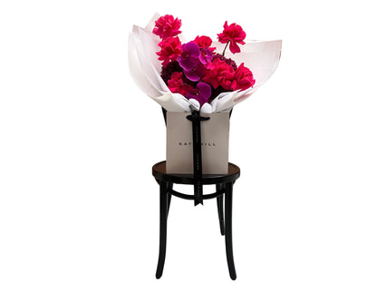 June signature flower bouquet featuring bright pink tones on black chair.