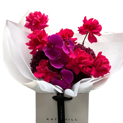 June signature flower bouquet featuring bright pink tones on black chair.