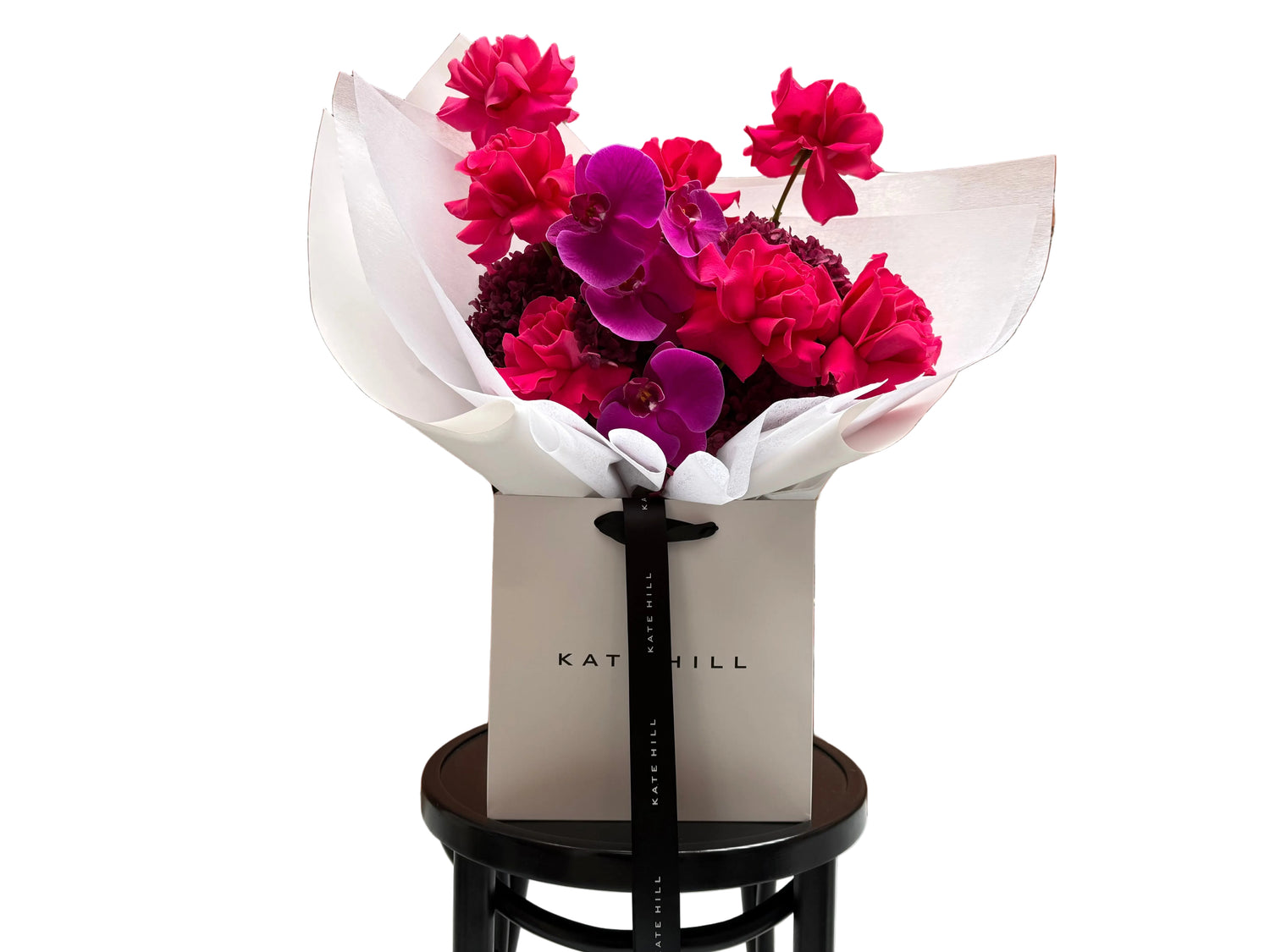 June signature flower bouquet featuring bright pink tones on black chair.