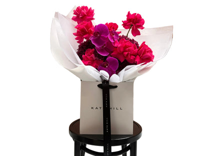 June signature flower bouquet featuring bright pink tones on black chair.