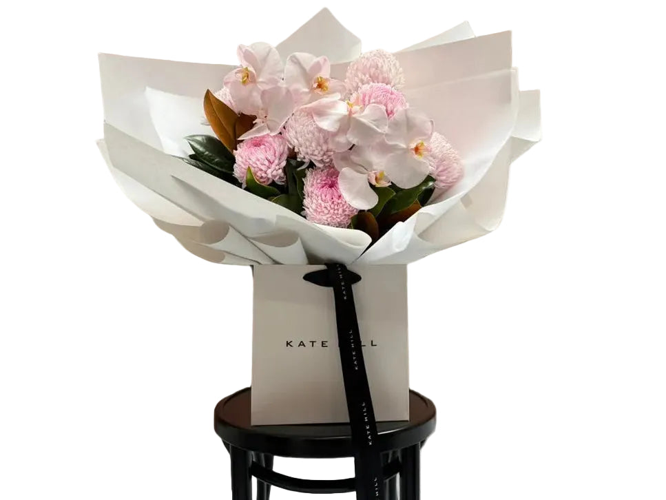 Large flower bouquet of blush pink flowers, beautifully wrapped in signature white paper and sitting in Kate Hill flower bag on black bentwood chair.