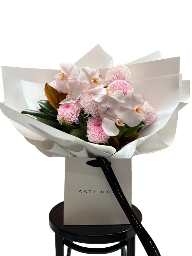 Large flower bouquet of blush pink flowers, beautifully wrapped in signature white paper and sitting in Kate Hill flower bag on black bentwood chair.