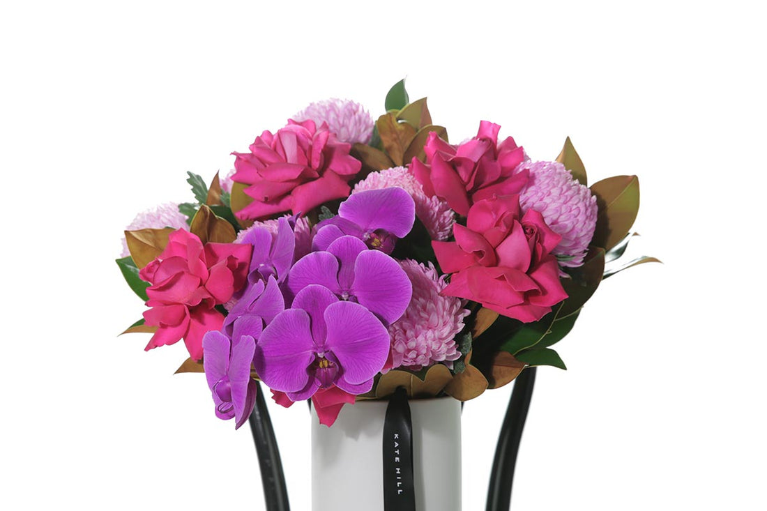Kate Hill Flowers – large hot-pink birthday vase with roses, disbuds, orchids and magnolia in a white ceramic cylinder.
