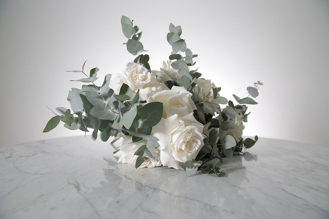 Bridal bouquet of white roses and eucalyptus on a marble surface with a light grey background