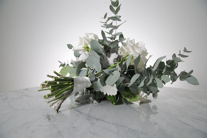 Bridal bouquet of white roses and eucalyptus on a marble surface with a light grey background