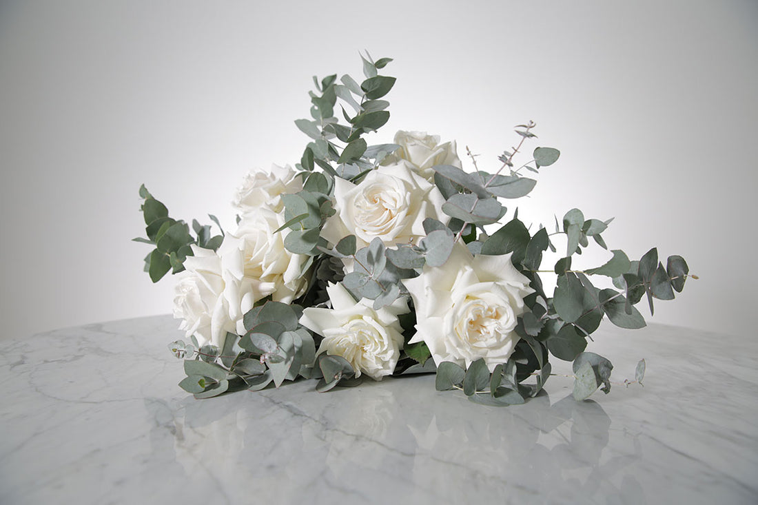 Bridal bouquet of white roses and eucalyptus on a marble surface with a light grey background