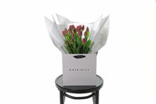 Kate Hill flower bag sitting on a black bentwood chair, displaying fresh premium pink tulip bouquet. Bouquet of 20 stems of pink barcelona tulips in image.