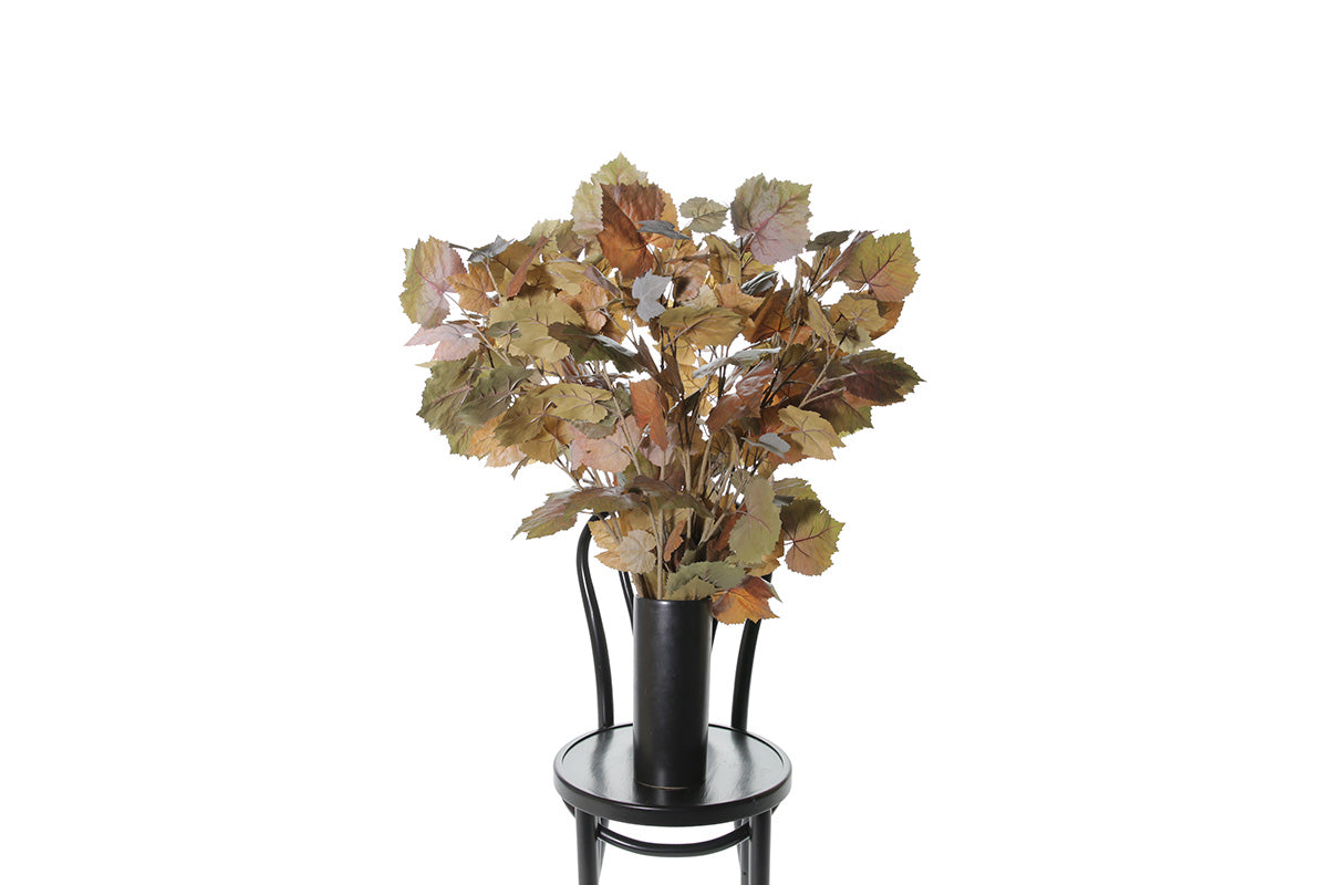 Artificial stems of faux maple foliage displayed in black vase that is sitting on black bentwood chair with a white background.