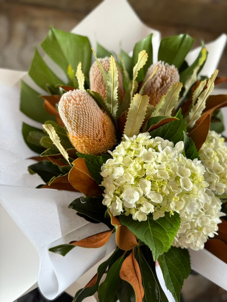 A close up of a florist holding a March birthday bouquet against a white wall.