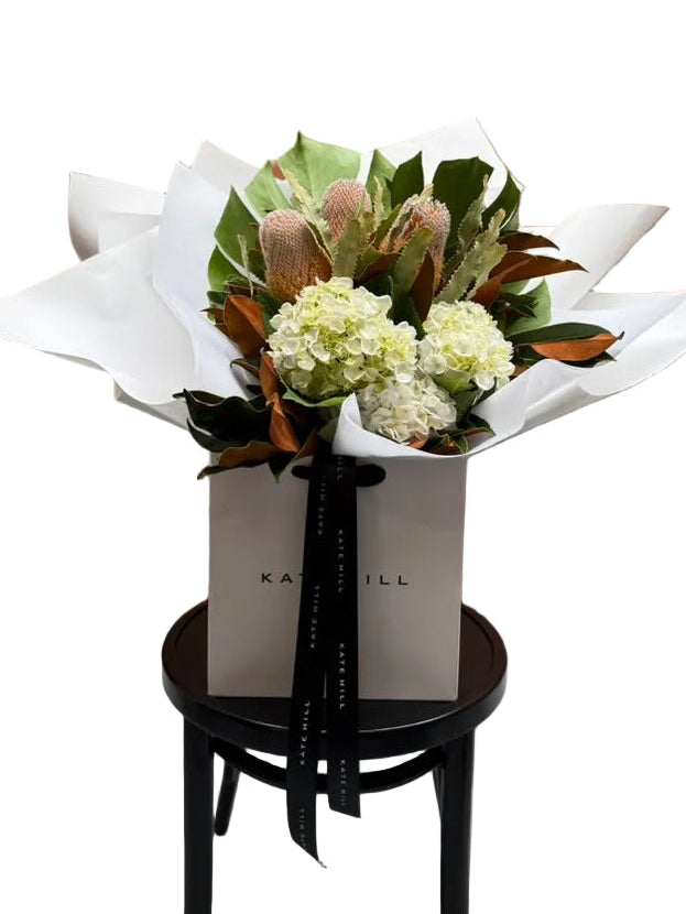 Our March birthday bouquet presented in a Kate Hill Flower Bag on a black bentwood chair against a white wall.