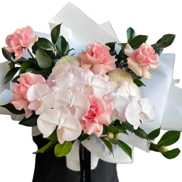 A close up image of a florist in black holding a large May Birthday Bouquet. Large Bouquet f flowers in soft blush tones, creams and green foliages. Bouquet wrapped in our signature white presentation.