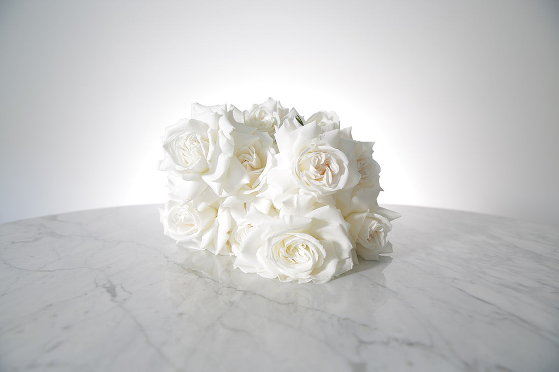 Reflexed white rose bridal bouquet with satin wrap and pearl pin finish placed on marble