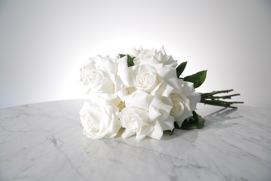 Reflexed white rose bridal bouquet with satin wrap and pearl pin finish placed on marble