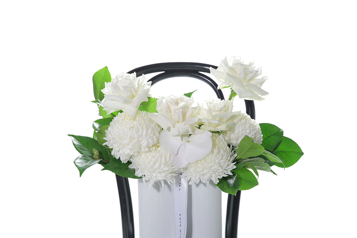 Kate Hill Flowers – medium white sympathy vase with roses, chrysanthemums, orchids and greenery in a wave-ceramic vessel.