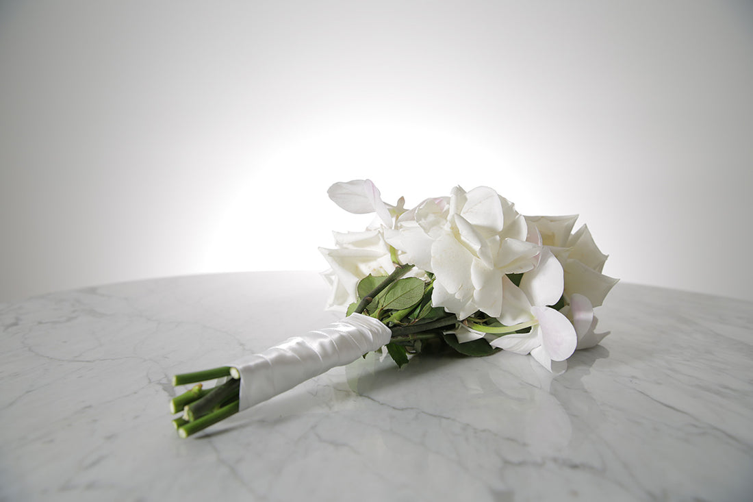 White reflexed rose and phalaenopsis orchid bridal bouquet bound in satin ribbon placed on a marble setting
