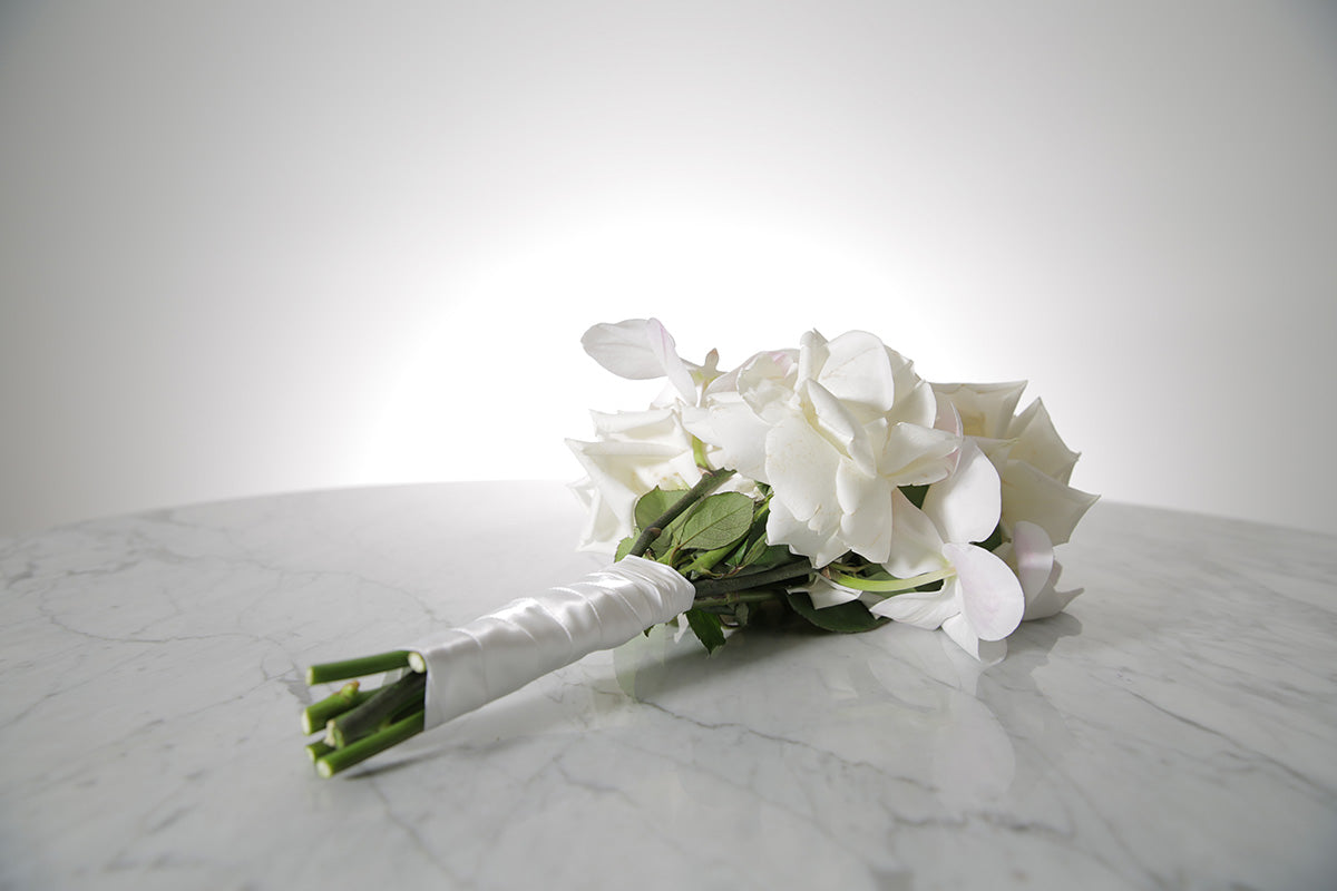 White reflexed rose and phalaenopsis orchid bridal bouquet bound in satin ribbon placed on a marble setting