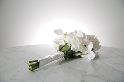 White reflexed rose and phalaenopsis orchid bridal bouquet bound in satin ribbon placed on a marble setting