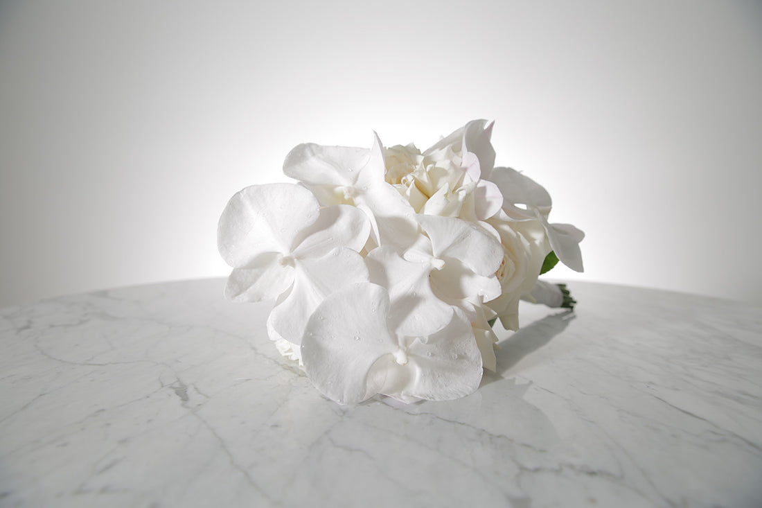 White reflexed rose and phalaenopsis orchid bridal bouquet bound in satin ribbon placed on a marble setting