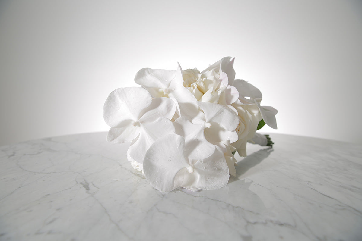 White reflexed rose and phalaenopsis orchid bridal bouquet bound in satin ribbon placed on a marble setting