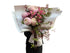 A soft pink flower bouquet of blush disbuds, sweet peas and jasmine foliage wrapped beautifully in signature white paper with Kate Hill ribbon. Florist holding bouquet against a white wall.