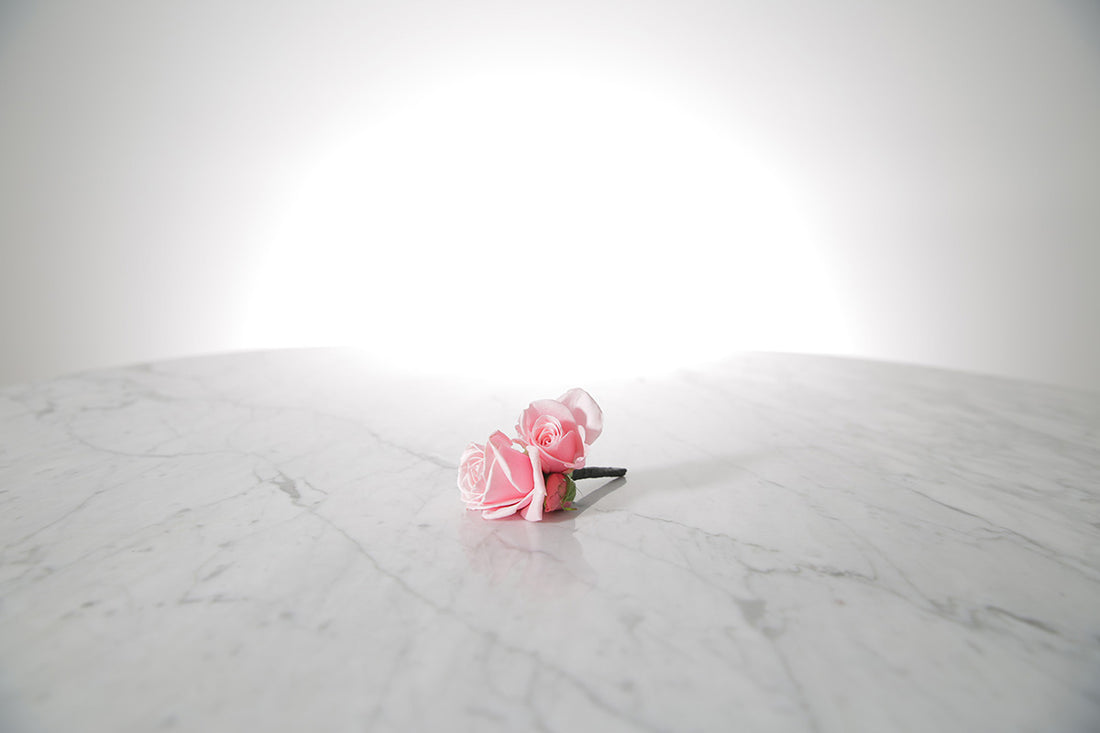 Kate Hill Flowers – pink spray rose buttonhole flowers with black-taped stem and pearl pin on a marble table setting.