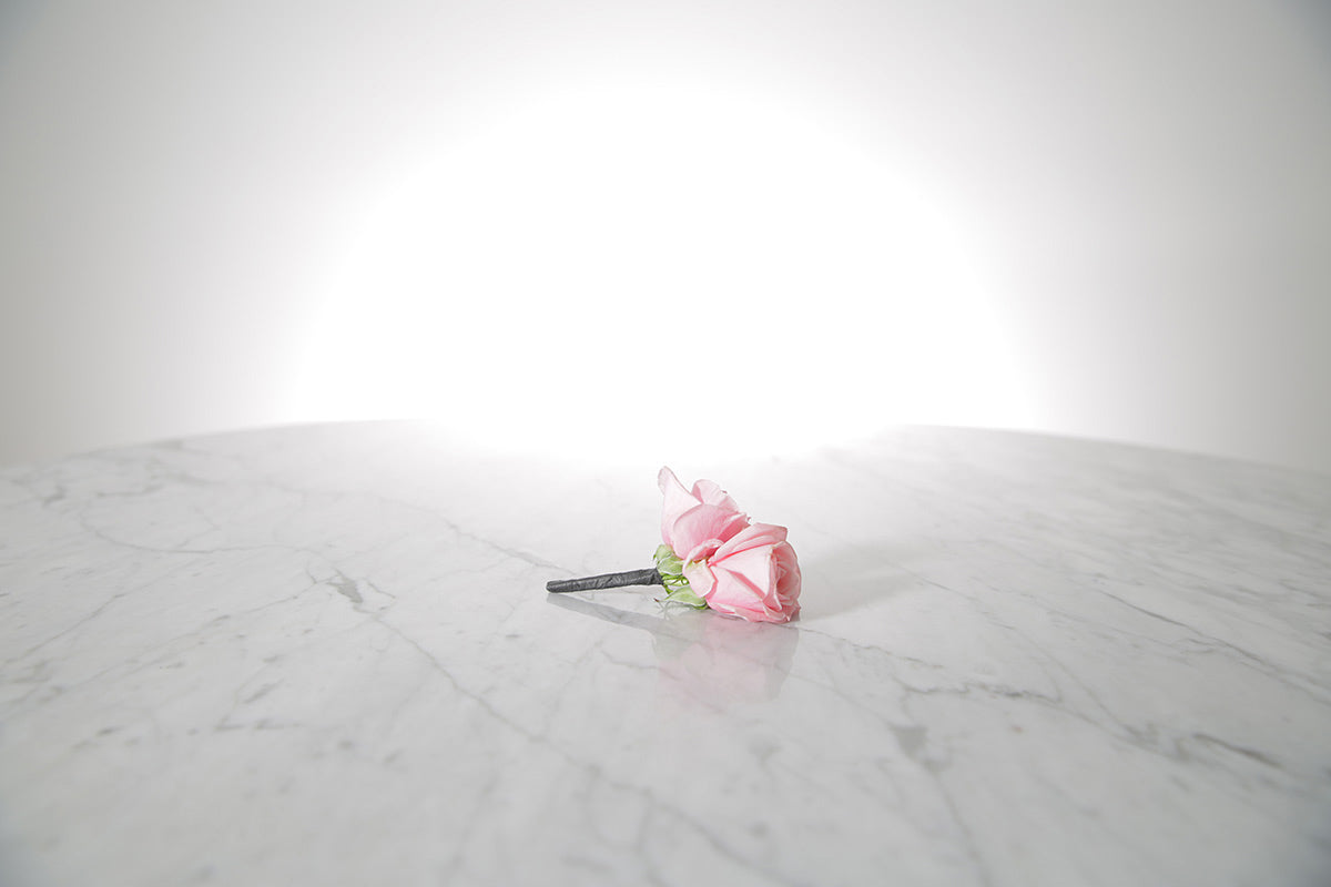 Kate Hill Flowers – pink spray rose buttonhole flowers with black-taped stem and pearl pin on a marble table setting.