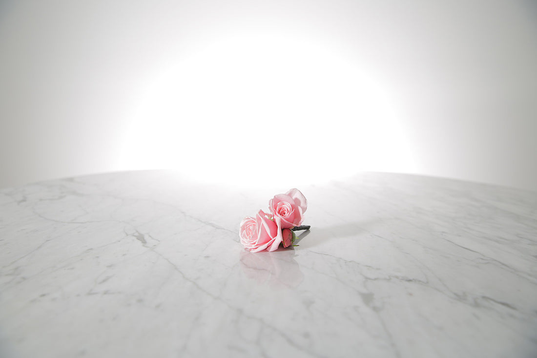 Kate Hill Flowers – pink spray rose buttonhole flowers with black-taped stem and pearl pin on a marble table setting.