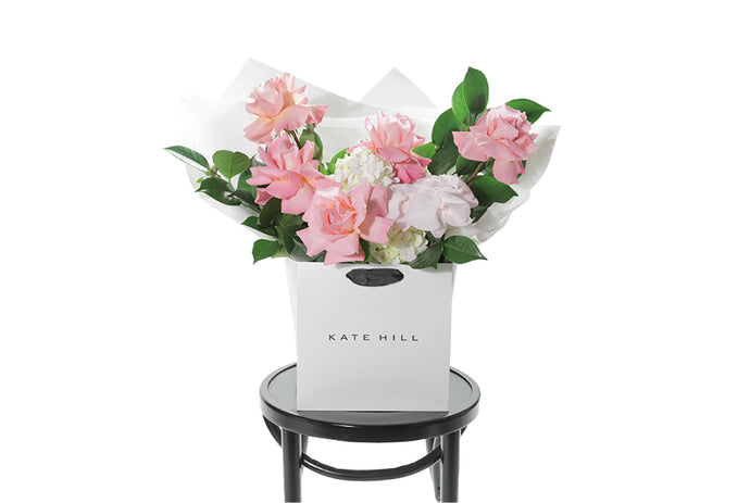 Large pastel pink, blush, white and green gift bouquet, beautifully wrapped in signature Kate Hill flowers wrapping, placed into our flower bag to ensure the bouquet stays fresh in water. Large in size. Bouquet bag is sitting on a black bentwood chair with white background.