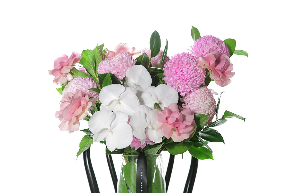 Kate Hill Flowers – large soft-pink celebration vase with roses, chrysanthemums and orchids in a monstera-lined glass.