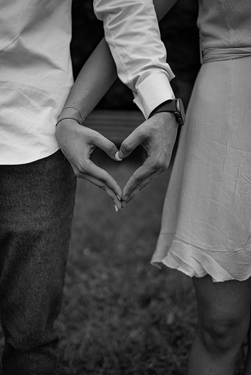 Two people forming a heart shape with their hands in a black and white photo.